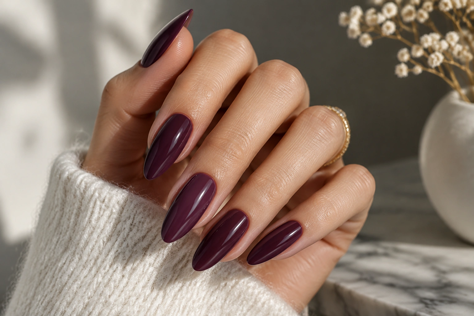 Hand with almond-shaped glossy plum nails on a neutral background